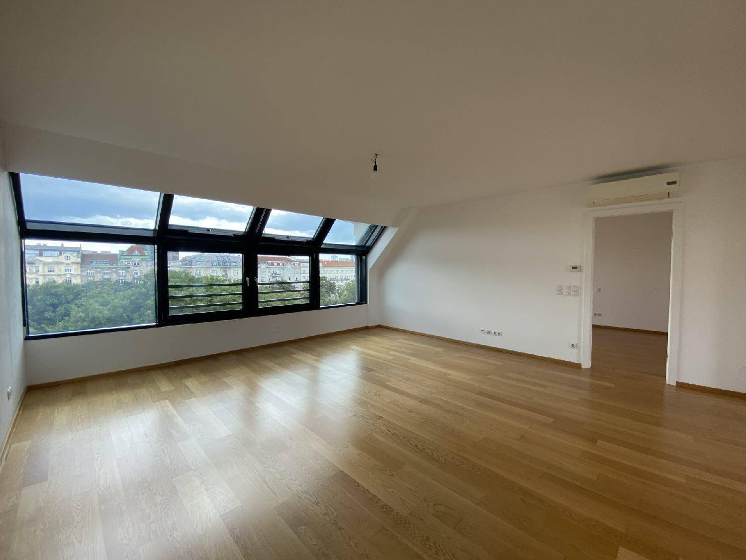 Geräumiger Wohnbereich mit großen Dachfenstern, Parkettboden und Blick auf die Stadt.