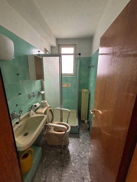 Schlichtes Badezimmer mit mintgrünen Fliesen, Dusche, WC, Bidet und Fenster.