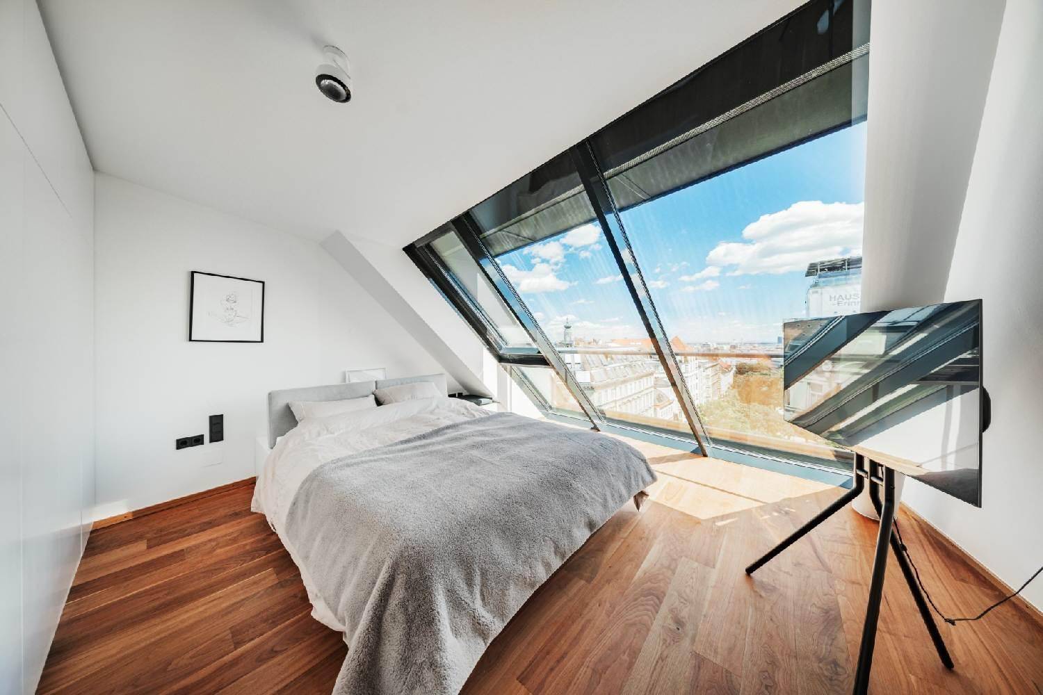 Modernes Schlafzimmer mit Holzboden, schrägen Fenstern und beeindruckendem Stadtblick.