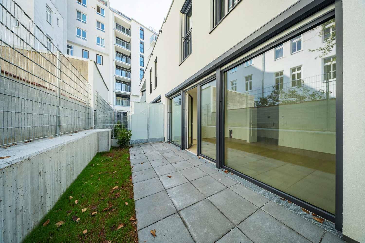 Moderne Terrasse mit Steinplatten und angrenzendem Rasenbereich vor dem Gebäude.