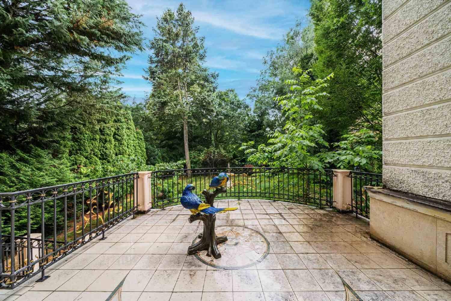 Geräumige Terrasse mit Fliesenboden und schmiedeeisernem Geländer, umgeben von üppigem Grün.