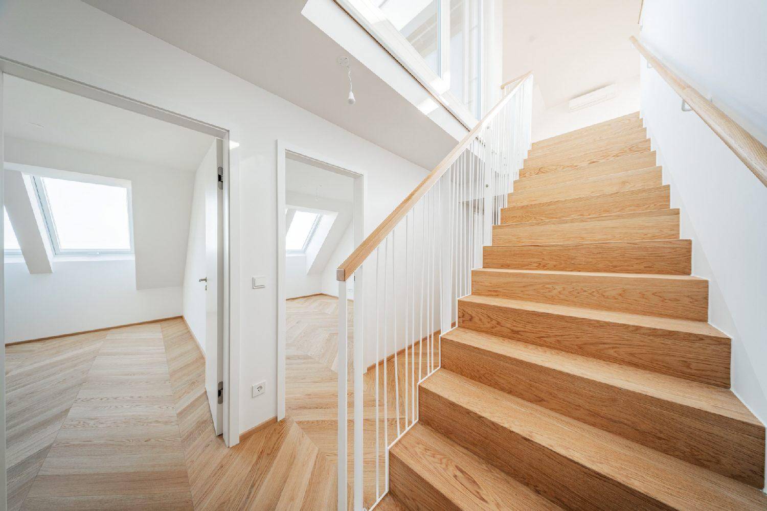 Modernes Treppenhaus mit Holzstufen und hellem Geländer, führt zu weiteren Räumen mit Parkettboden.