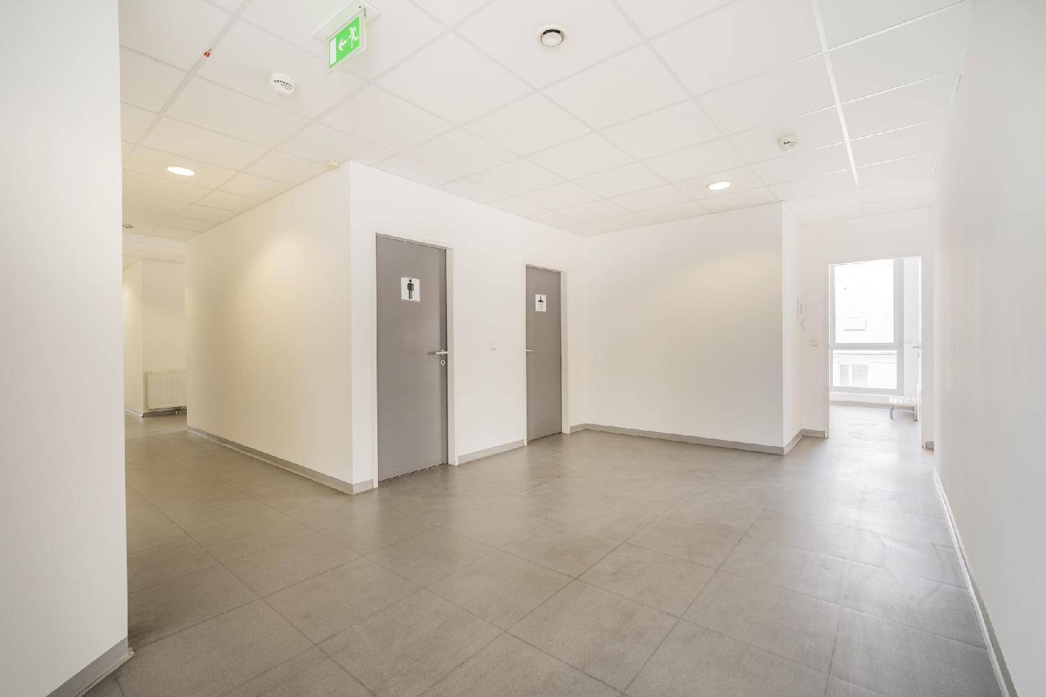 Heller Flur mit grauen Fliesen und zwei Türen, die zu den Toilettenbereichen führen.