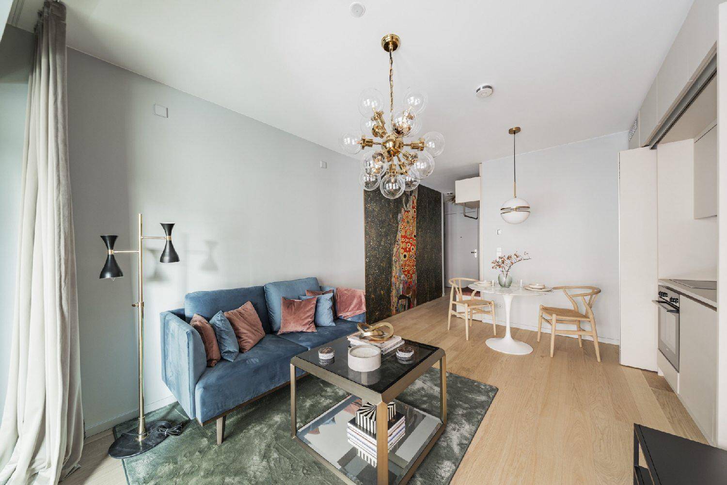 Helles Wohnzimmer mit blauer Couch, Esstisch und integrierter Küchenzeile in modernem Stil.