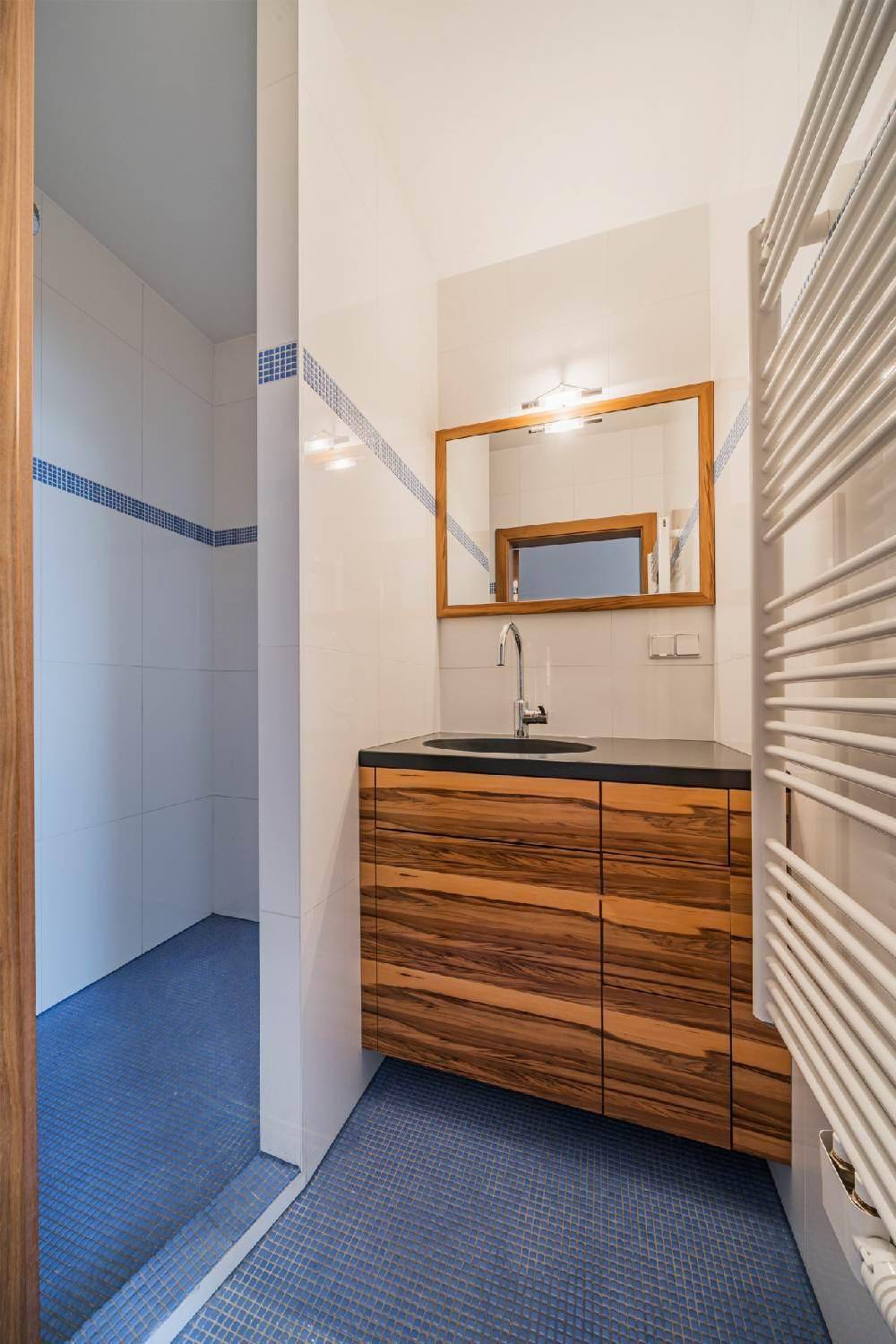 Modernes Badezimmer mit blauen Mosaikfliesen, Holzwaschtisch und Dusche.