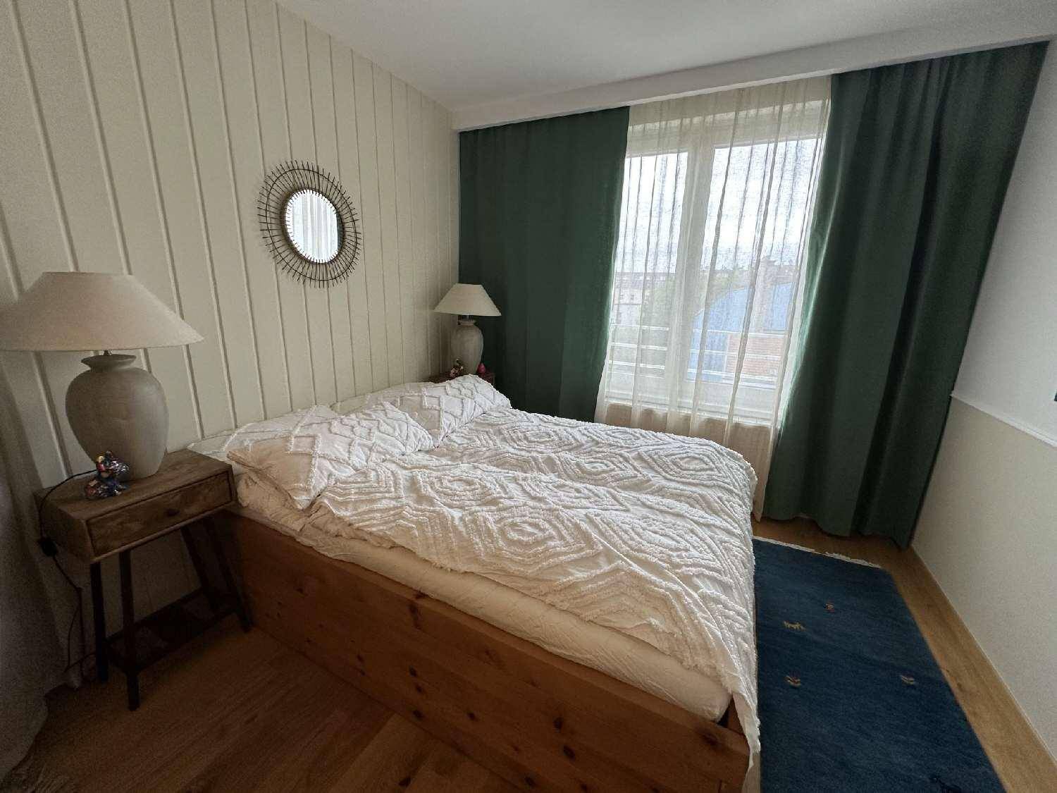 Helles Schlafzimmer mit Holzbett, Nachttischen, grünen Vorhängen und Holzboden.