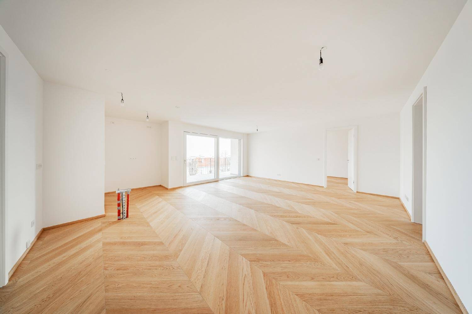 Großzügiger, heller Wohnraum mit elegantem Fischgrät-Parkettboden und breiter Fensterfront zum Außenbereich.