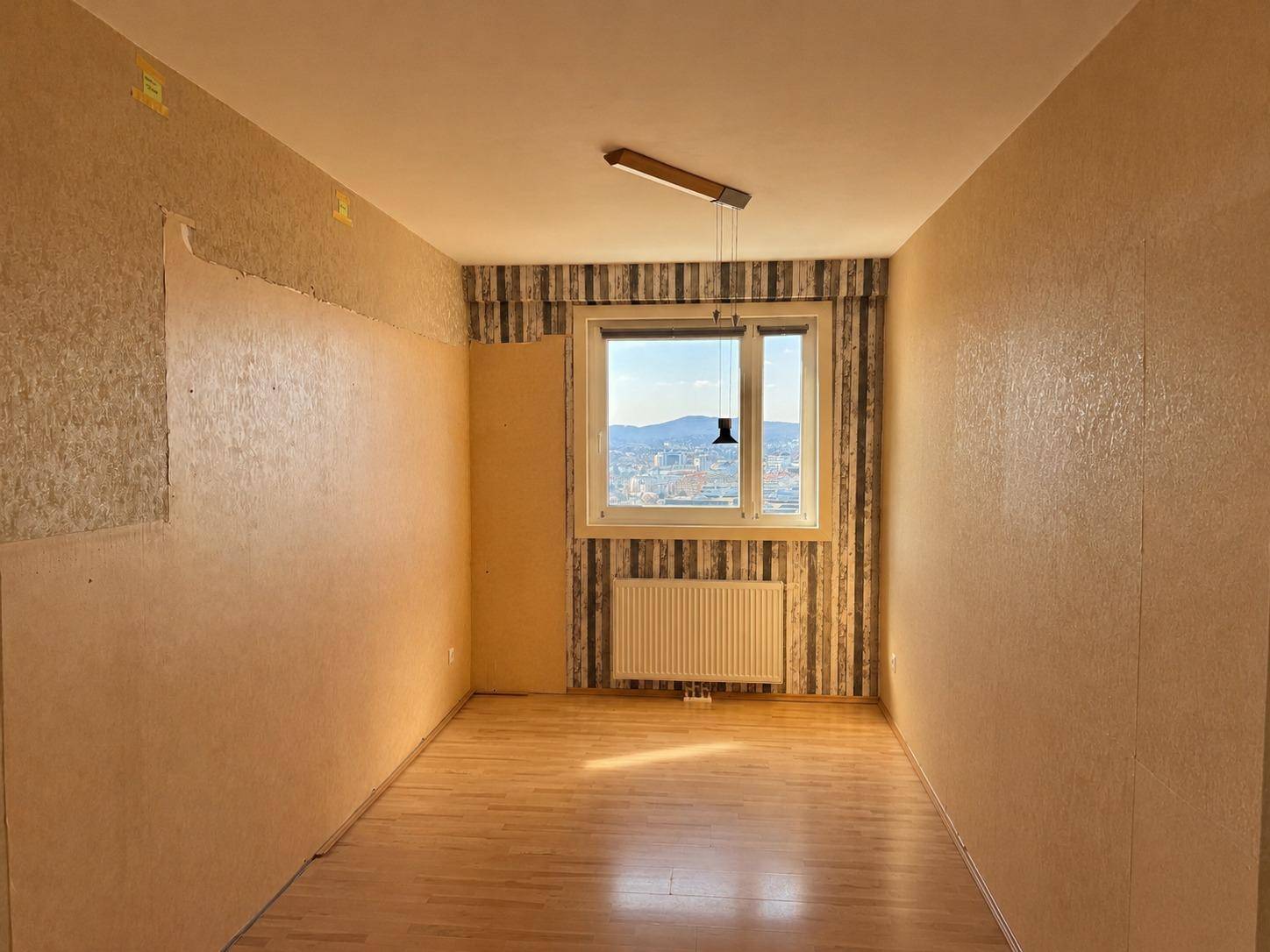 Zimmer mit Parkettboden und einem Fenster, das einen weiten Blick über die Stadt ermöglicht.