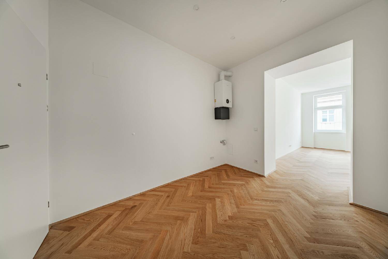 Raum mit Fischgrätparkett und einem Wandheizkessel, der die Wärmeversorgung des Apartments sicherstellt.