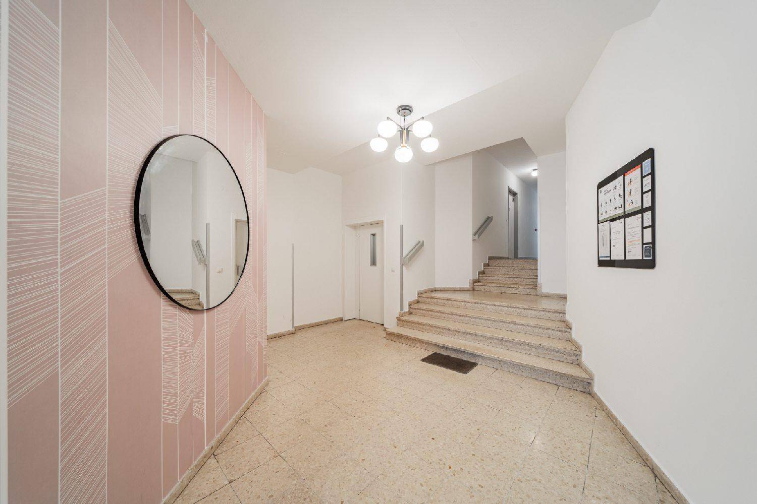 Eingangsbereich des Gebäudes mit Terrazzoboden, Treppe und dekorativer Wandgestaltung.