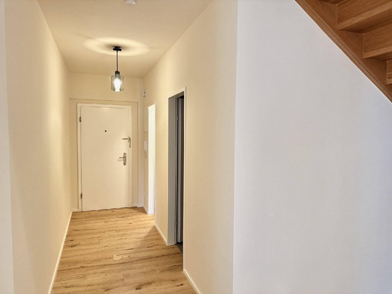 Heller Flur mit Holzboden, Eingangstür, Aufzug und Holztreppe zum Obergeschoss.