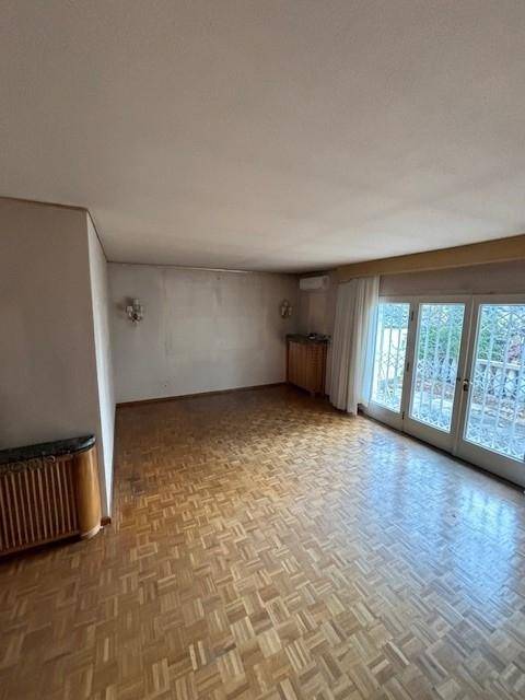 Weitläufiges Wohnzimmer mit Parkettboden und großen Fenstertüren zum Gartenbereich.
