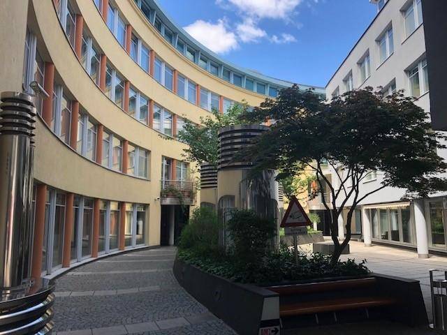 Attraktiver Innenhof mit geschwungener Gebäudefassade, Bäumen und gepflastertem Boden, bietet eine grüne Oase.