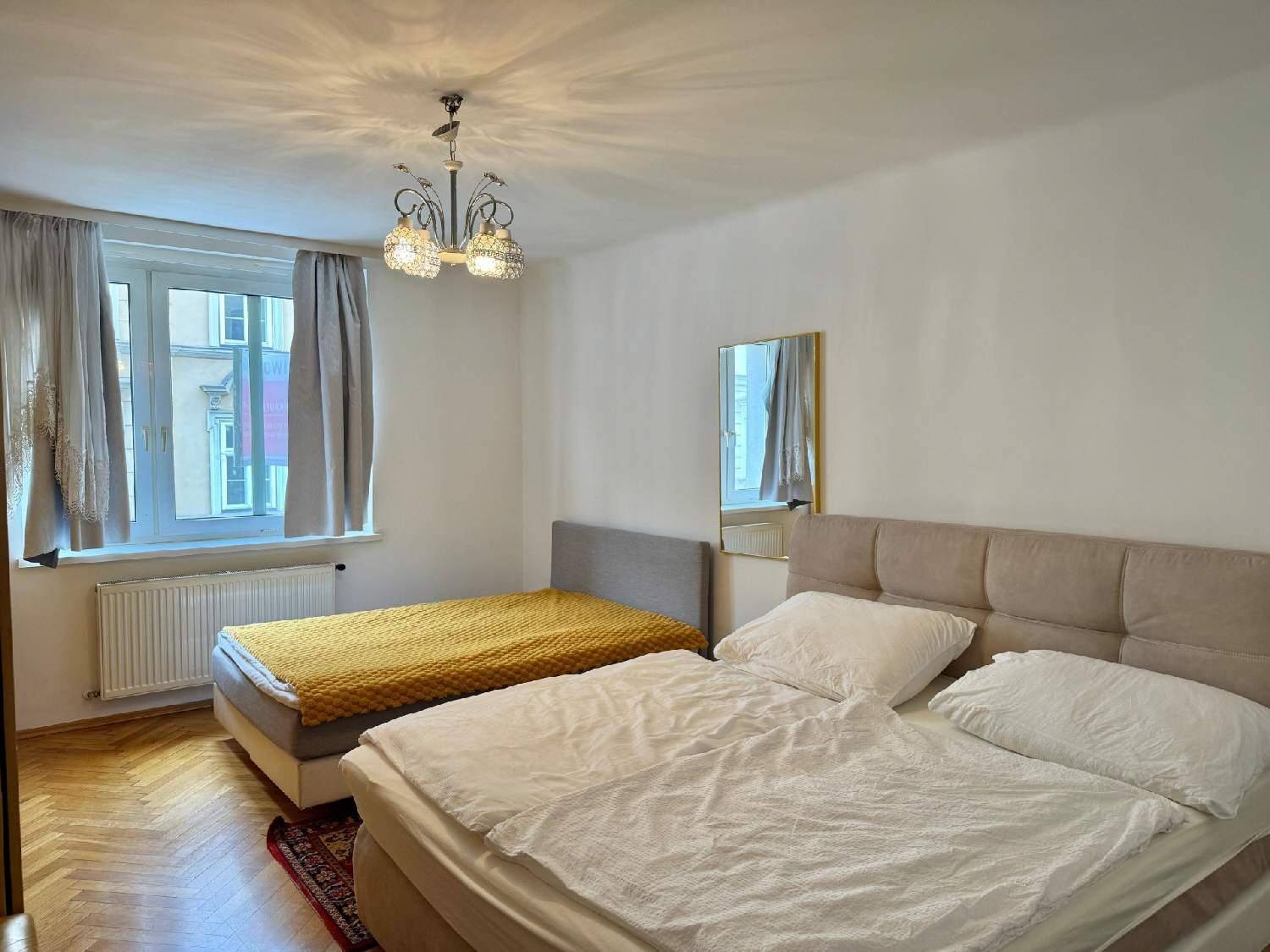 Schlafzimmer mit zwei Betten, Fischgrätparkett und Fenster mit Vorhängen.