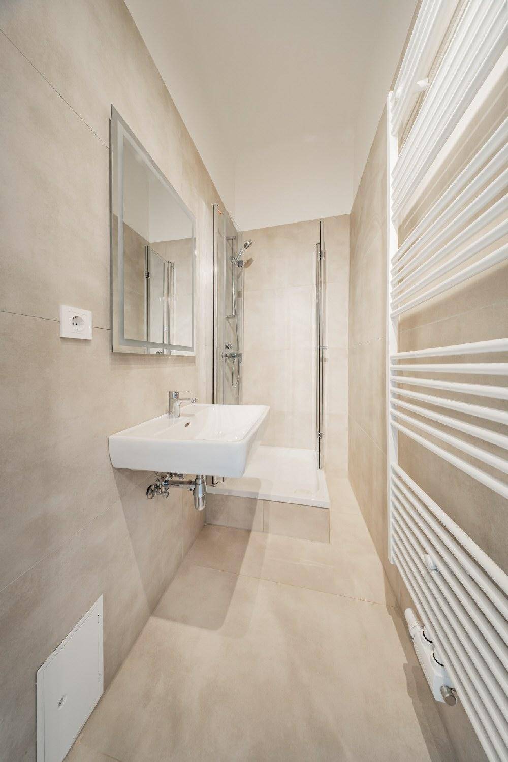 Modernes Badezimmer mit beigefarbenen Fliesen, Einzelwaschbecken, Dusche und beheiztem Handtuchhalter.