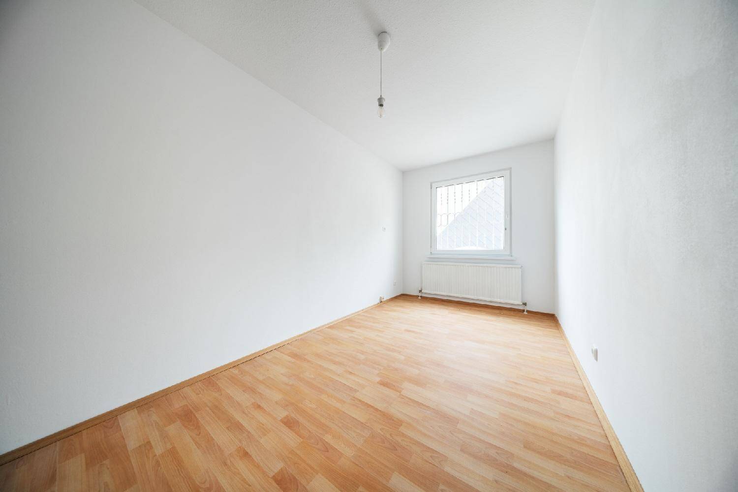Helles, leeres Zimmer mit Laminatboden und Fenster, ideal als Schlaf- oder Arbeitszimmer.