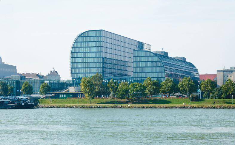 Modernes Bürogebäude am Flussufer mit markanter Architektur und grüner Umgebung.
