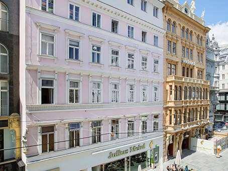Ansicht einer charmanten rosa Gebäudefassade mit vielen Fenstern in einer belebten Stadtstraße.