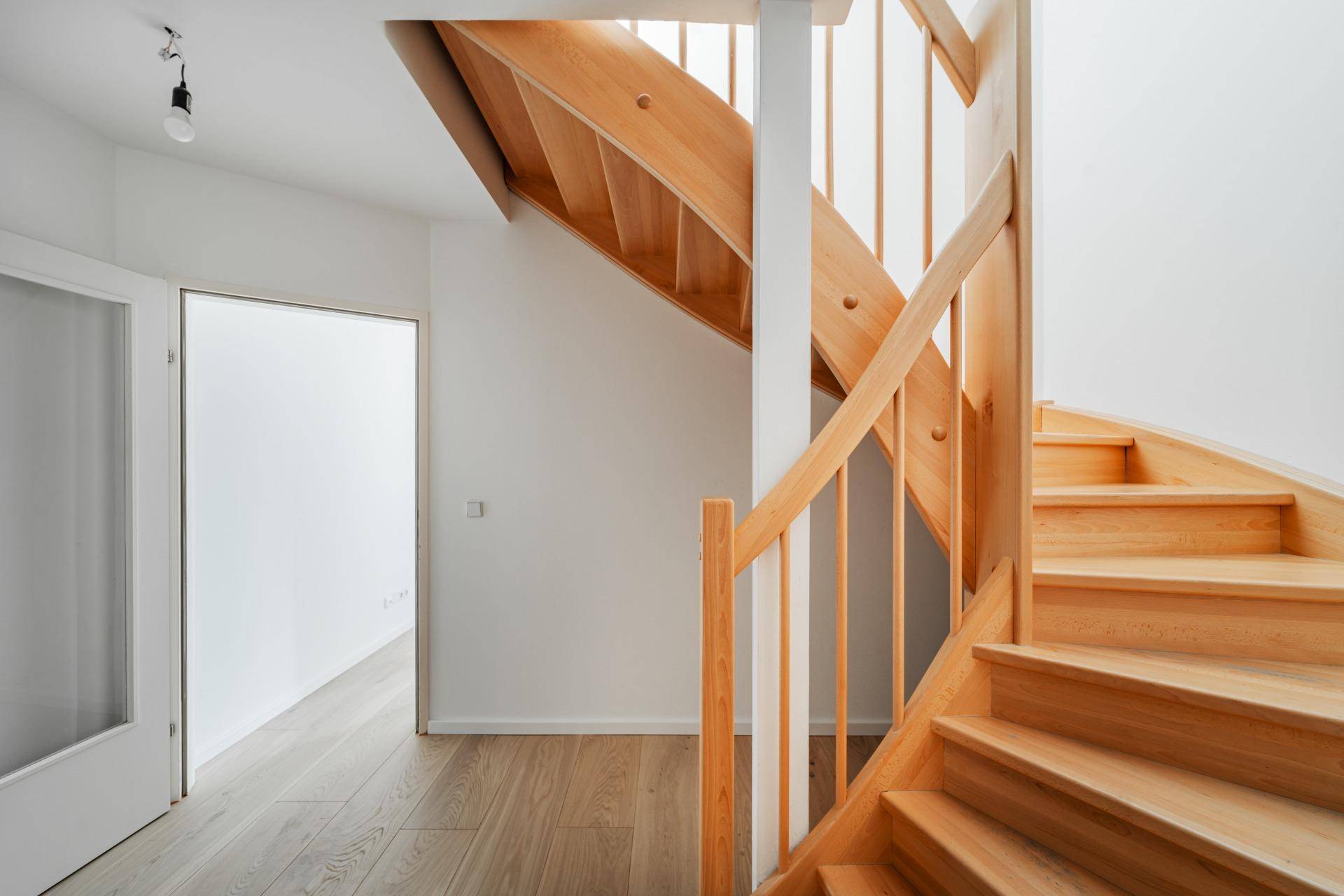 Helles Treppenhaus mit einer eleganten Holztreppe und passendem Parkettboden, das zu weiteren Räumen führt.