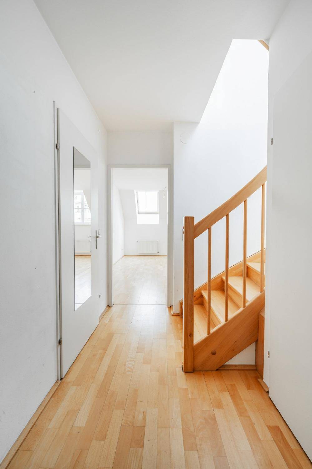 Langer Flur mit Holzfußboden und Treppe, der zu weiteren Zimmern mit Dachschrägen führt.