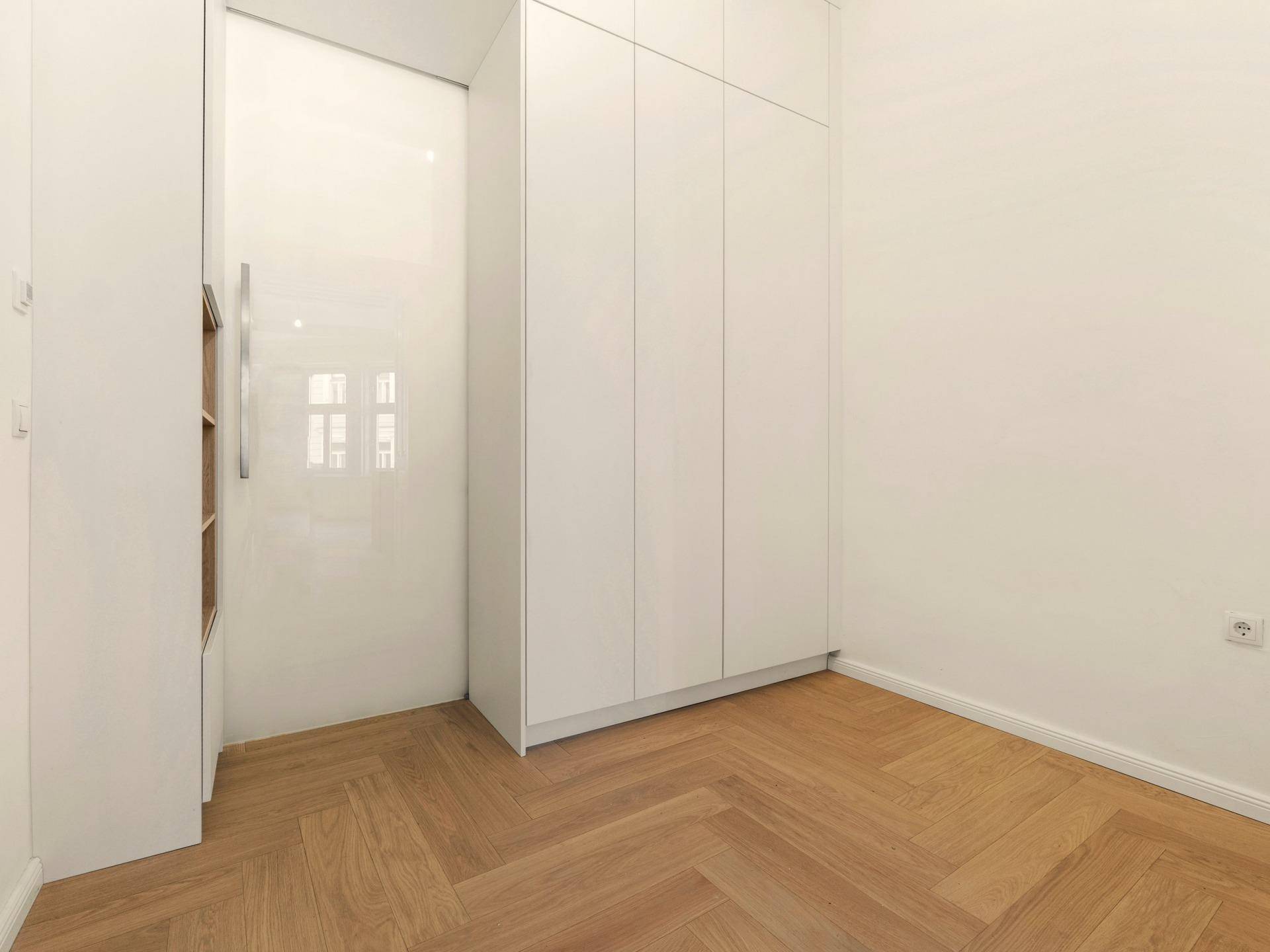 Raum mit weißen Einbauschränken und Fischgrätparkett, ideal als Ankleide oder Abstellraum.