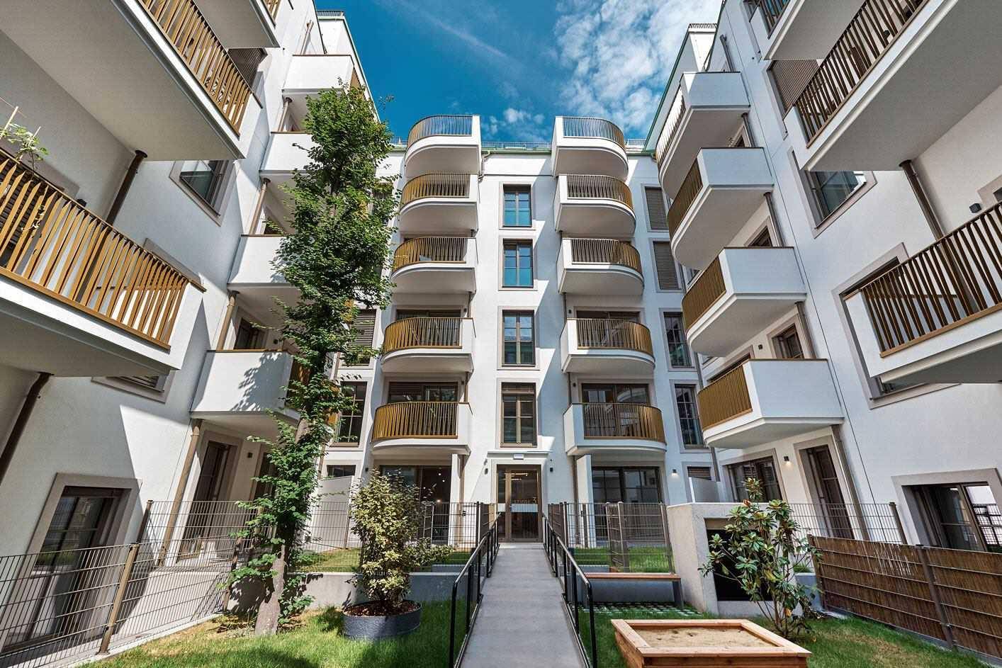 Innenhof mit gepflegtem Garten, Bäumen und modernen Balkonen der Wohnanlage.