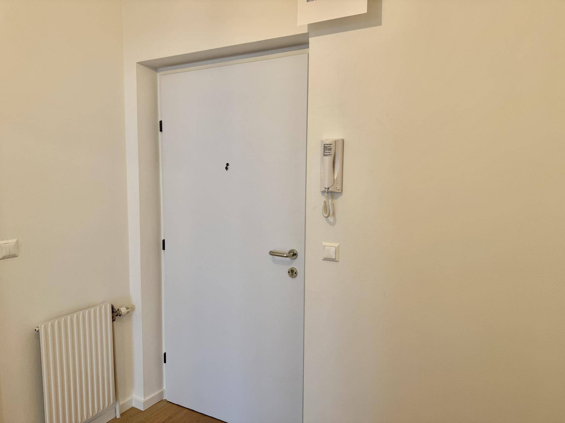 Eingangsbereich mit weißer Wohnungstür, Gegensprechanlage und Heizkörper.