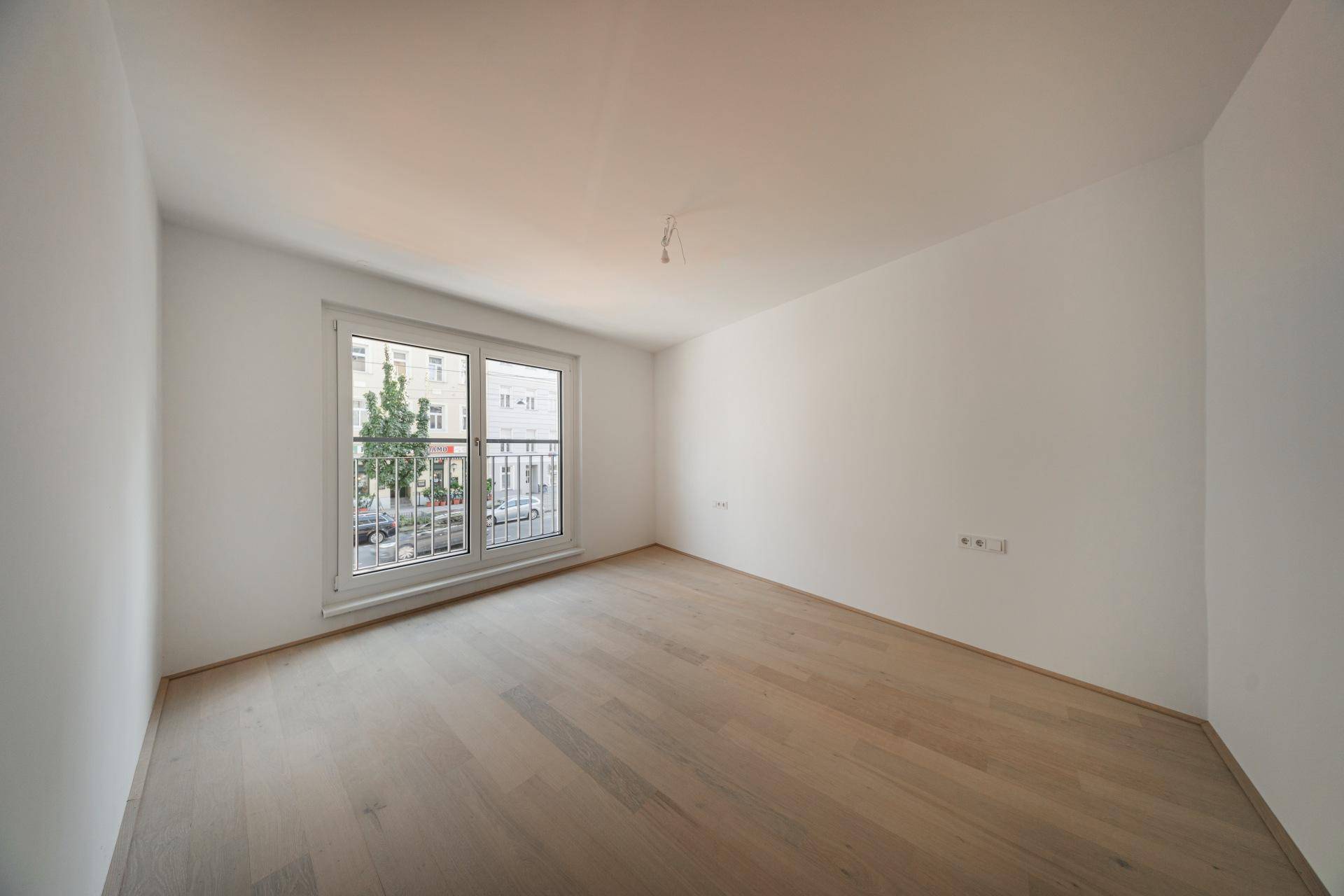 Helles Schlafzimmer mit Holzboden und einem französischen Balkon mit Blick auf die Straße.