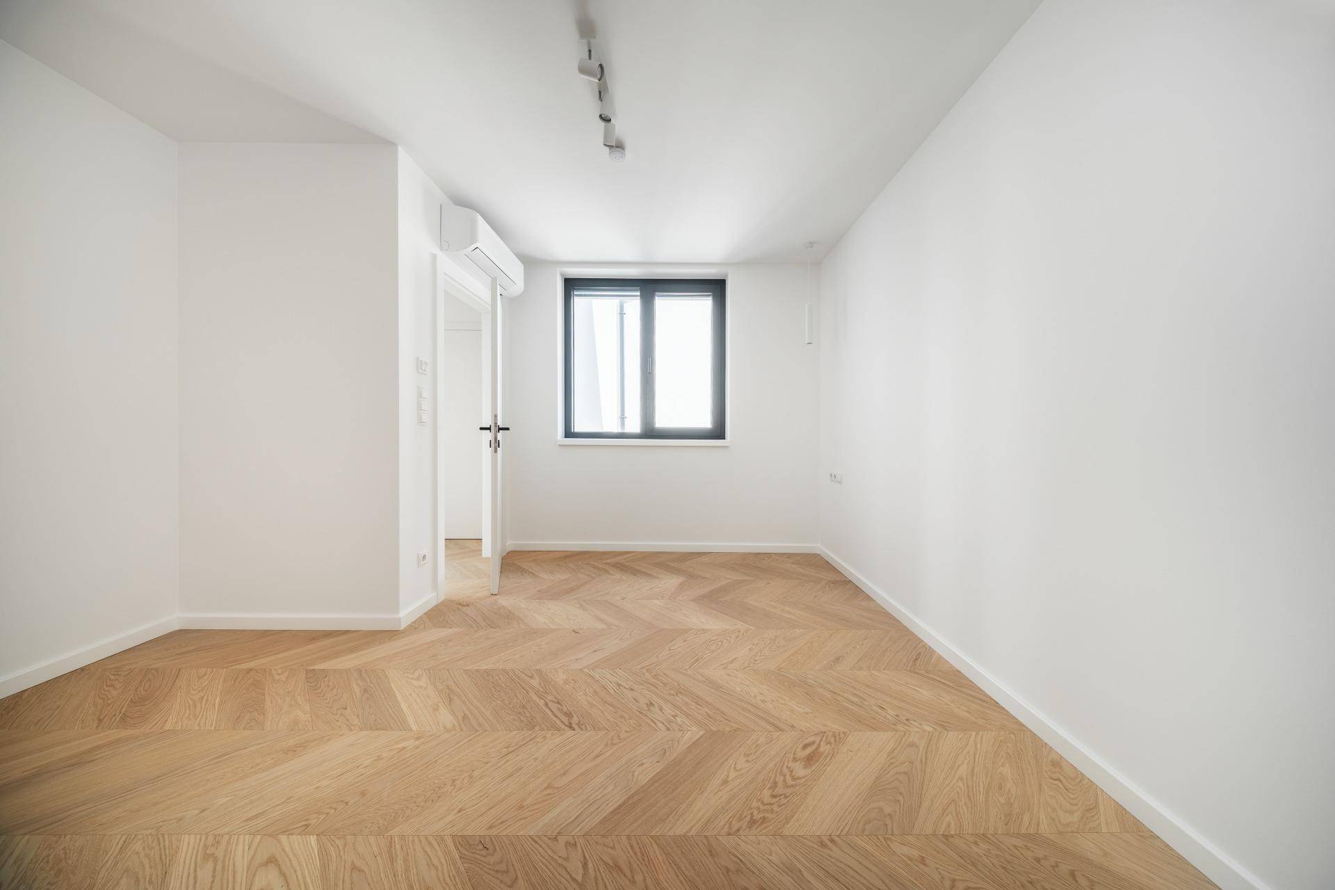 Geräumiges Schlafzimmer mit hellem Fischgrätparkett und moderner Klimaanlage an der Wand.