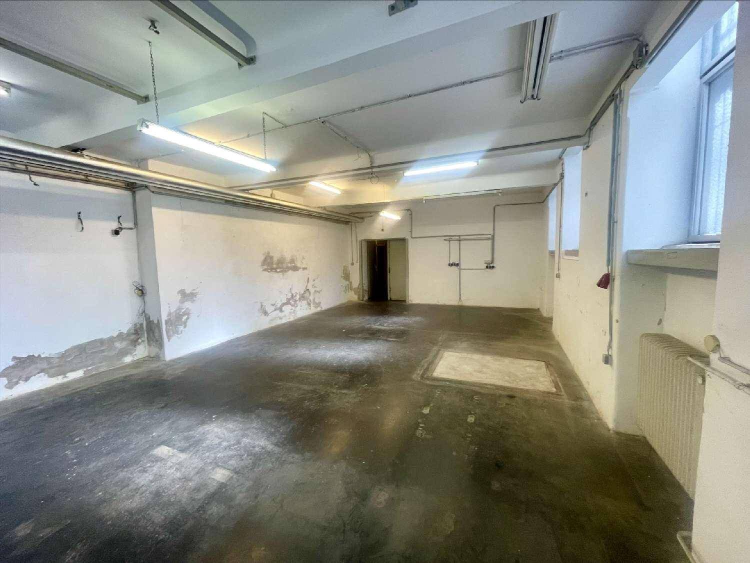 Großer, leerer Lagerraum mit hohen Decken, sichtbaren Rohren und Fenstern, die Tageslicht hereinlassen.