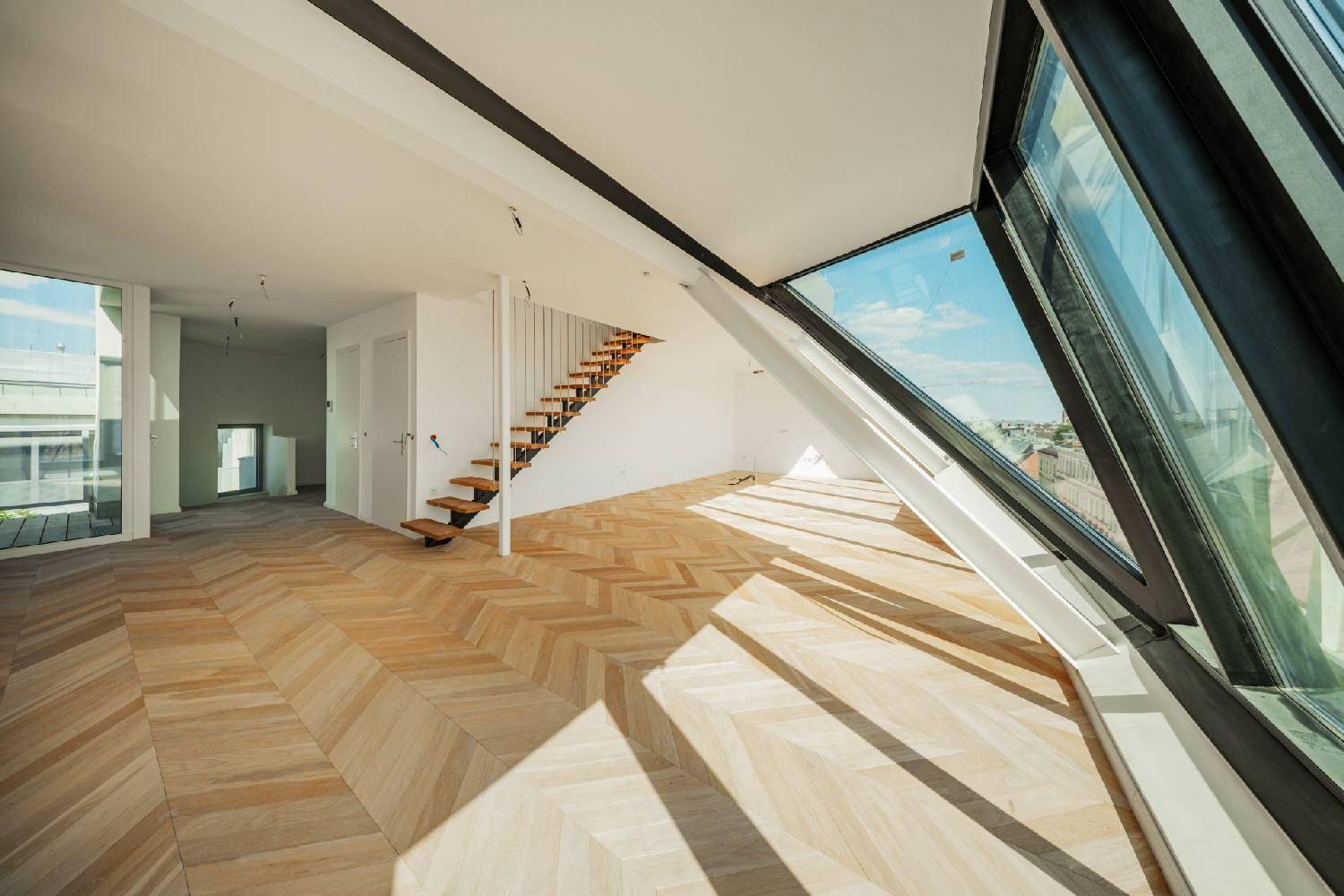 Geräumiger Wohnbereich mit Fischgrätparkett, großen Fenstern und Zugang zu einem Balkon.
