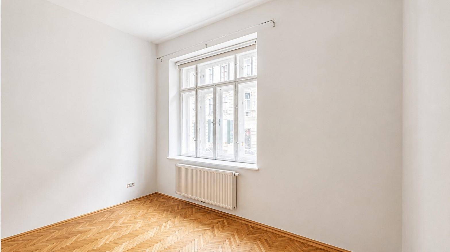 Lichtdurchflutetes Zimmer mit klassischem Fischgrätparkett und großem Fenster.