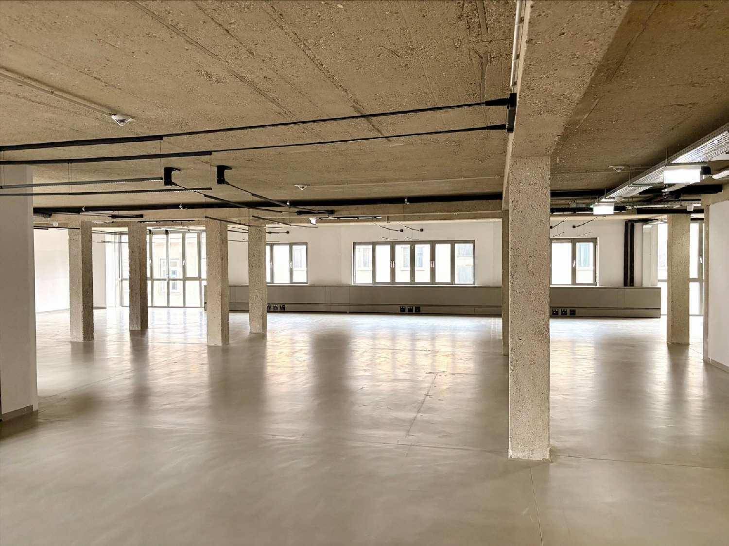 Heller, offener Büroraum mit vielen Fenstern, Betonsäulen und minimalistischem Design.