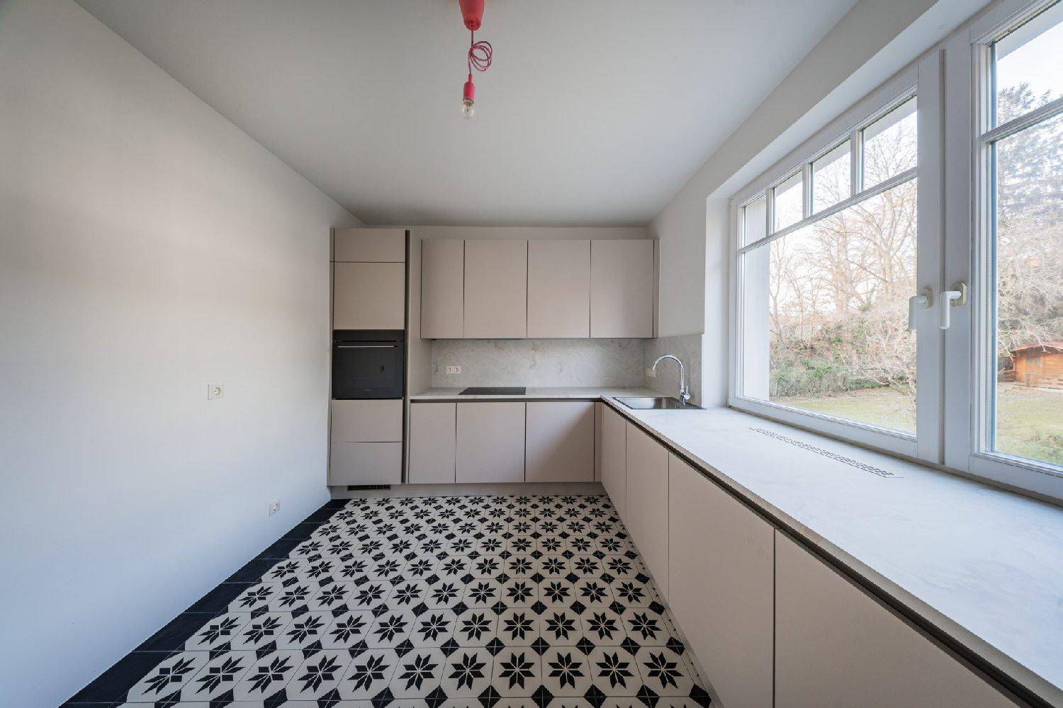 Moderne Einbauküche mit hellen Schränken, integrierten Geräten und großem Fenster mit Ausblick.