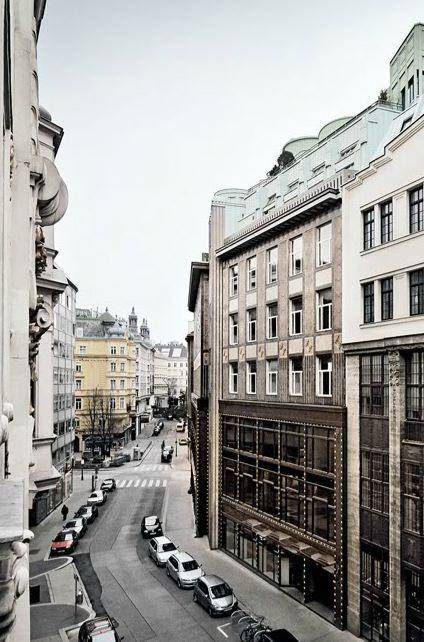 Belebtes Stadtbild mit historischen Gebäuden, geparkten Autos und Fußgängern auf der Straße.