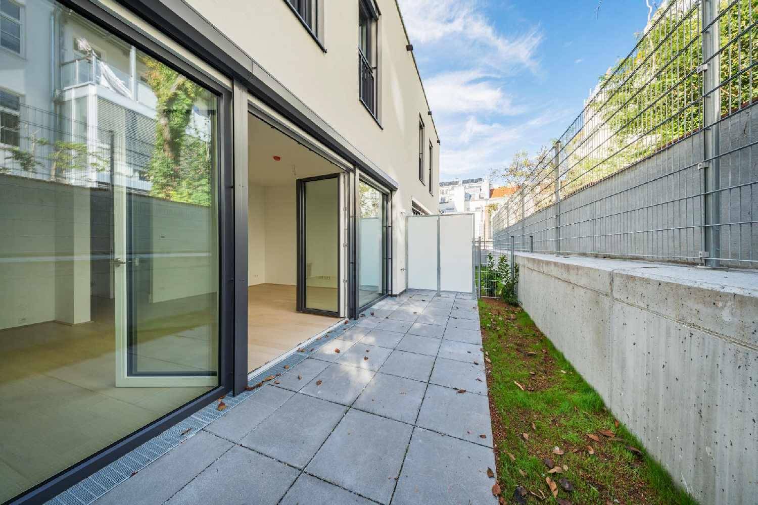 Moderne Terrasse mit Steinplatten und angrenzender Grünfläche, umgeben von einer Betonmauer.