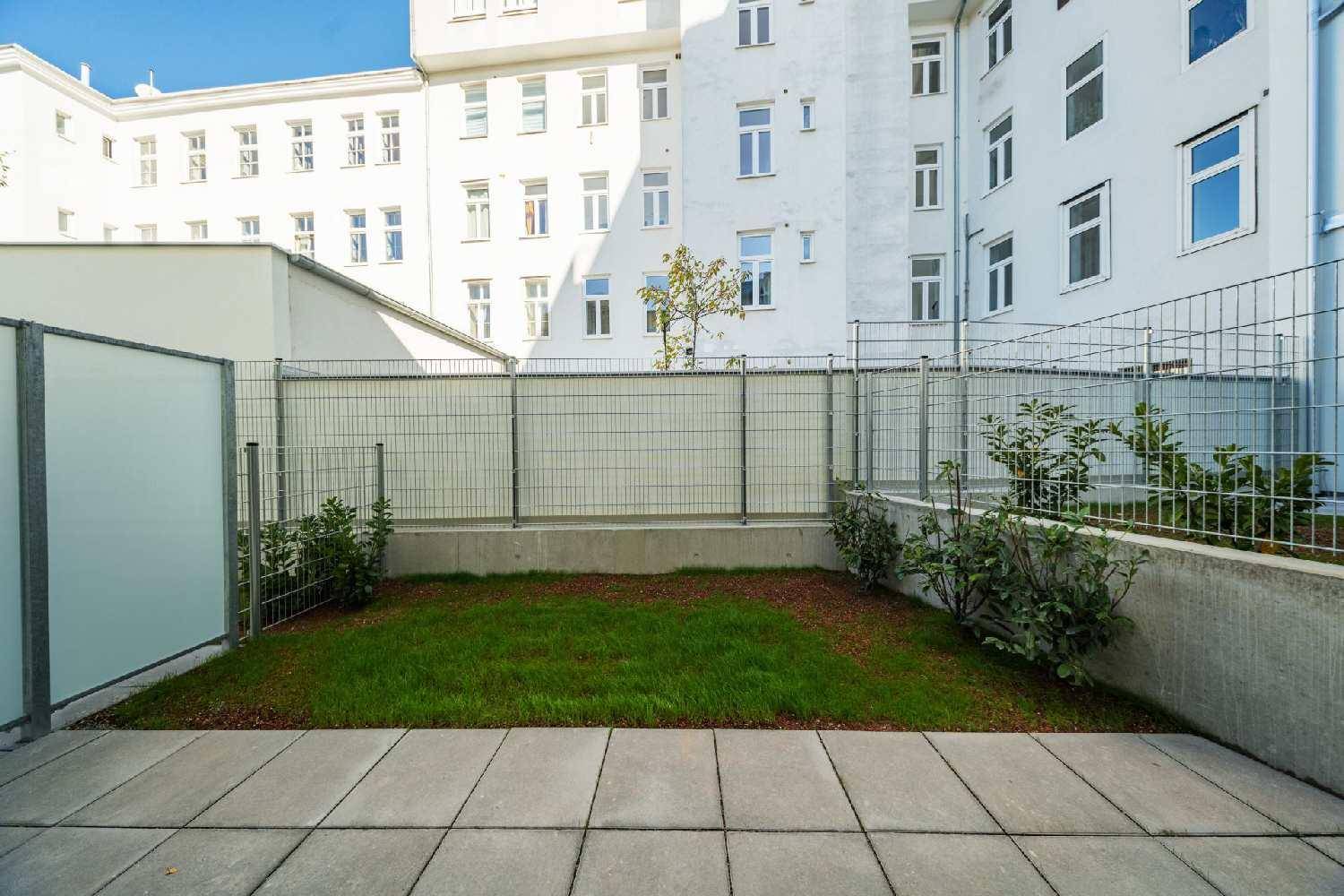 Kleiner, gepflegter Gartenbereich mit Rasenfläche und gepflasterter Terrasse, umgeben von einem Zaun.
