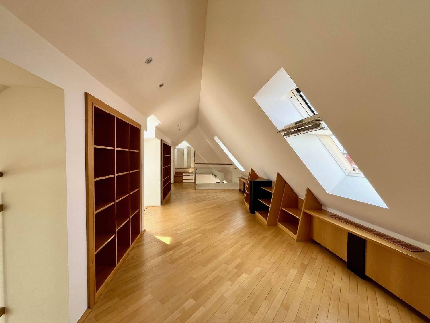 Heller Flur im Dachgeschoss mit Holzboden, Einbauregalen und mehreren Dachfenstern.