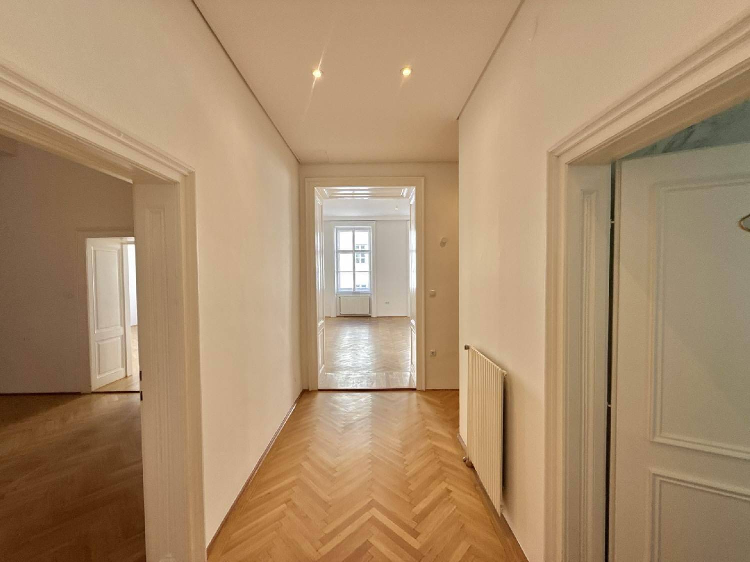 Langer Flur mit Fischgrätparkettboden, der zu weiteren hellen Räumen der Wohnung führt.
