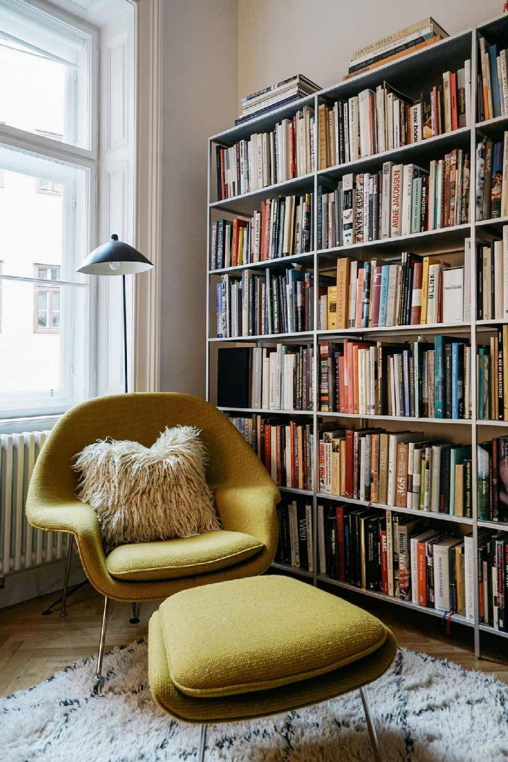 Gemütliche Leseecke mit einem gelben Sessel, Fußhocker und raumhohen Bücherregalen.