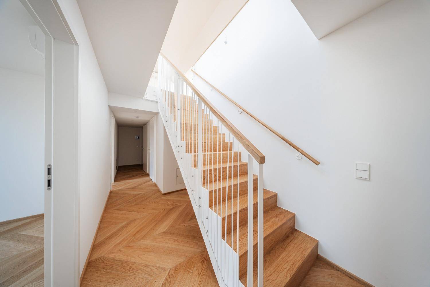 Helles Treppenhaus mit Holzstufen und modernem Geländer, verbindet die Etagen des Neubaus.