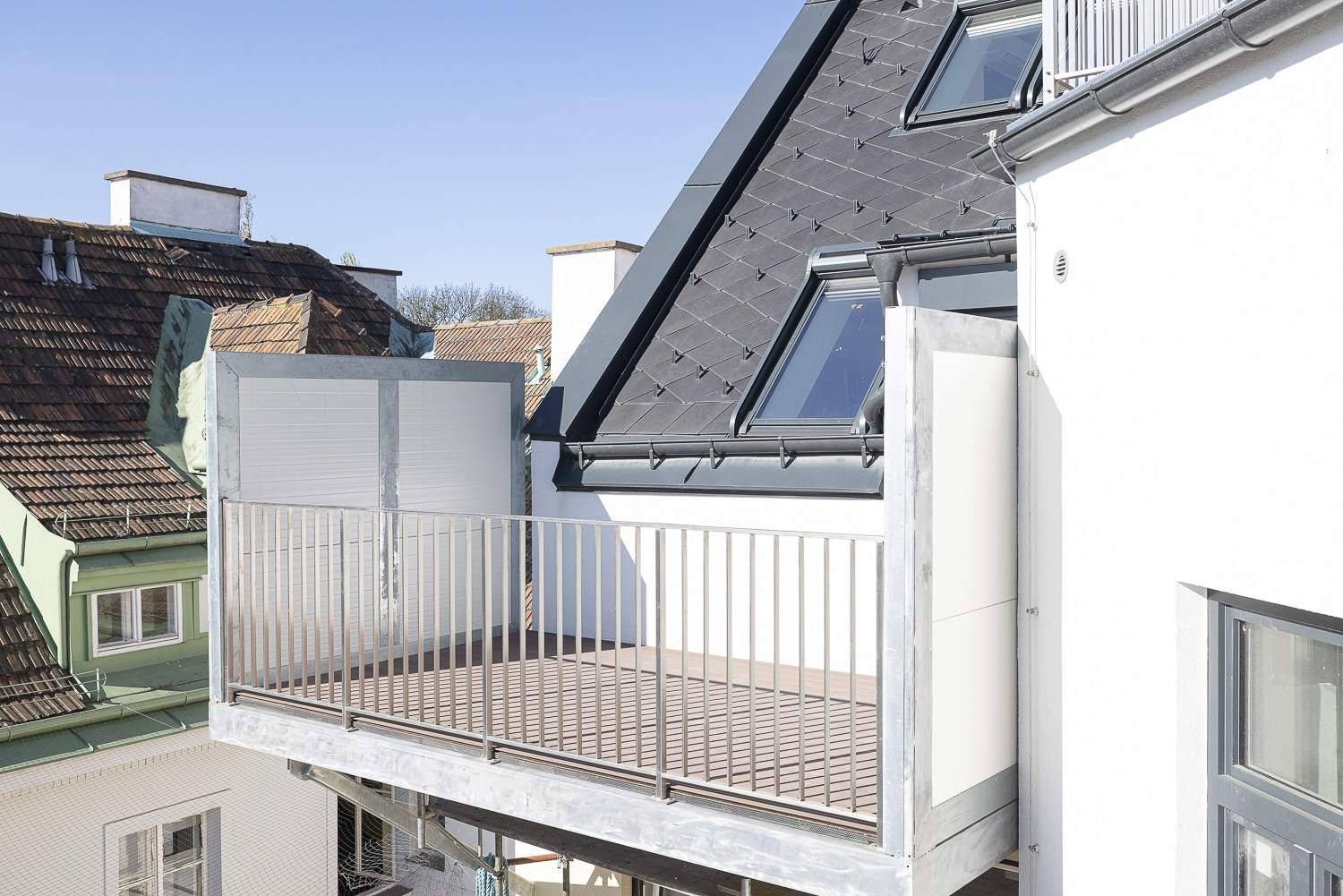 Außenansicht einer modernen Terrasse mit Metallgeländer und Dachfenstern im Hintergrund.