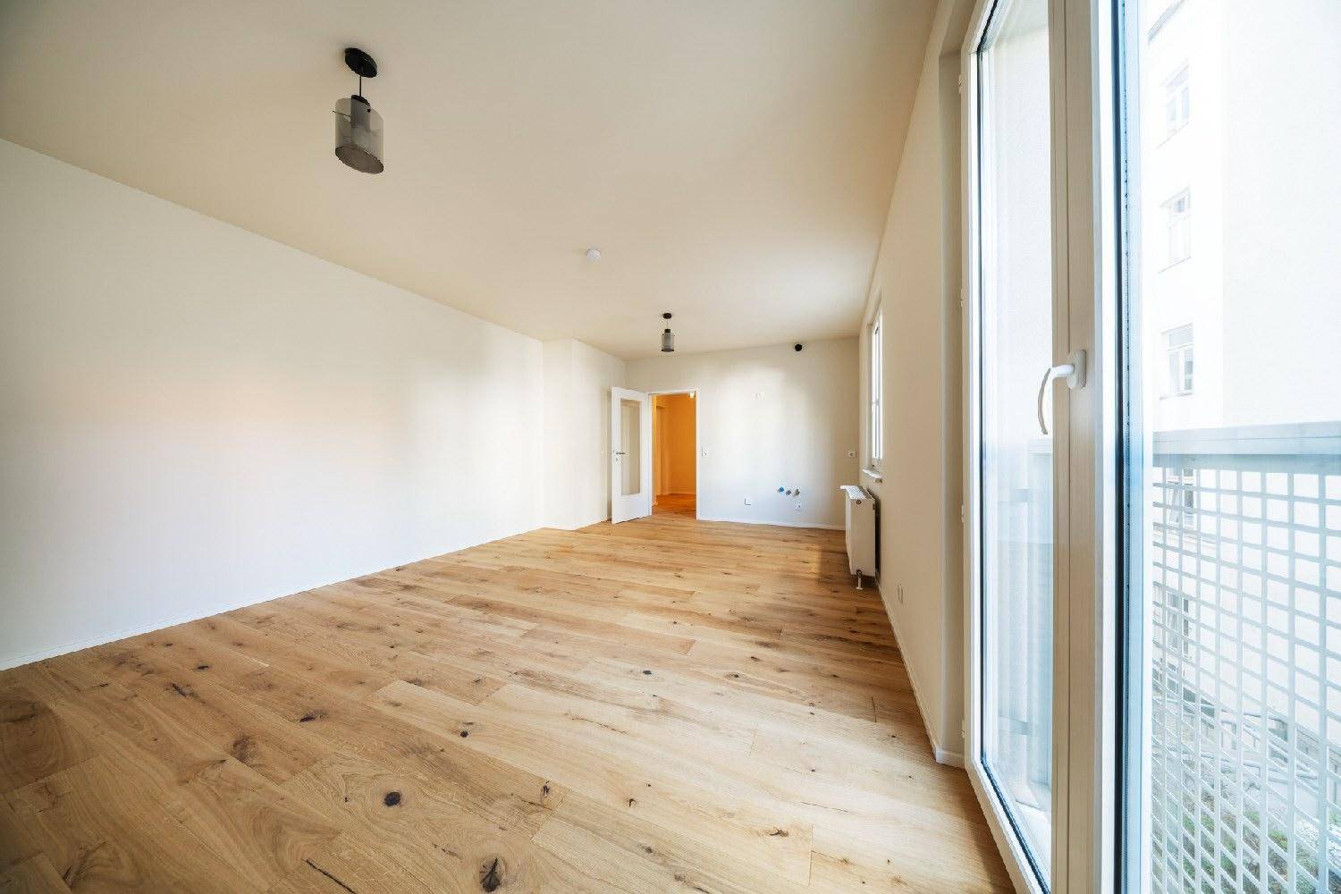 Geräumiges, helles Zimmer mit Holzboden, großen Fenstern und direktem Zugang zum Balkon.