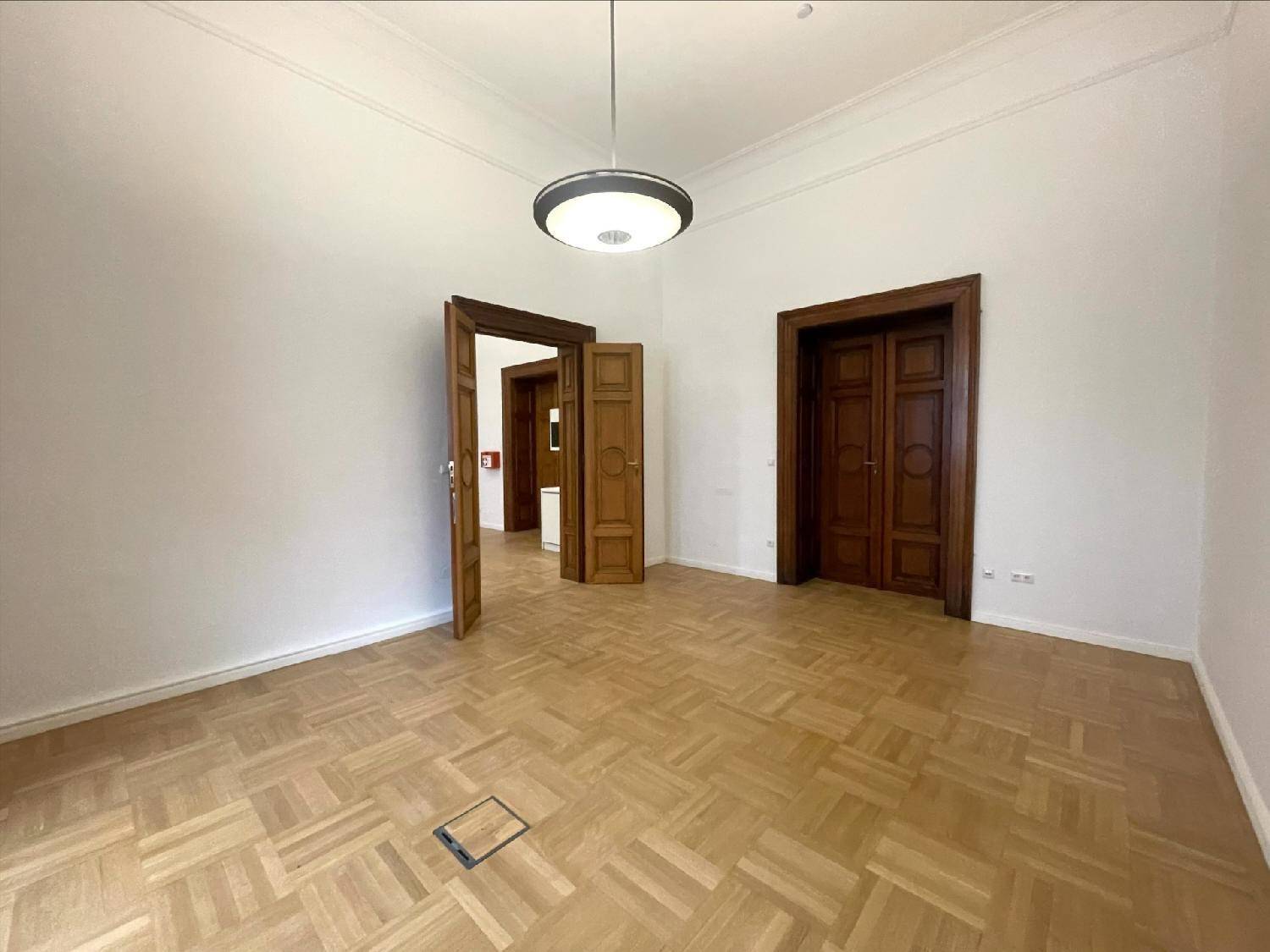 Geräumiger Innenraum mit hohen Decken, Fischgrätparkett und eleganten Holztüren, die zu angrenzenden Räumen führen.