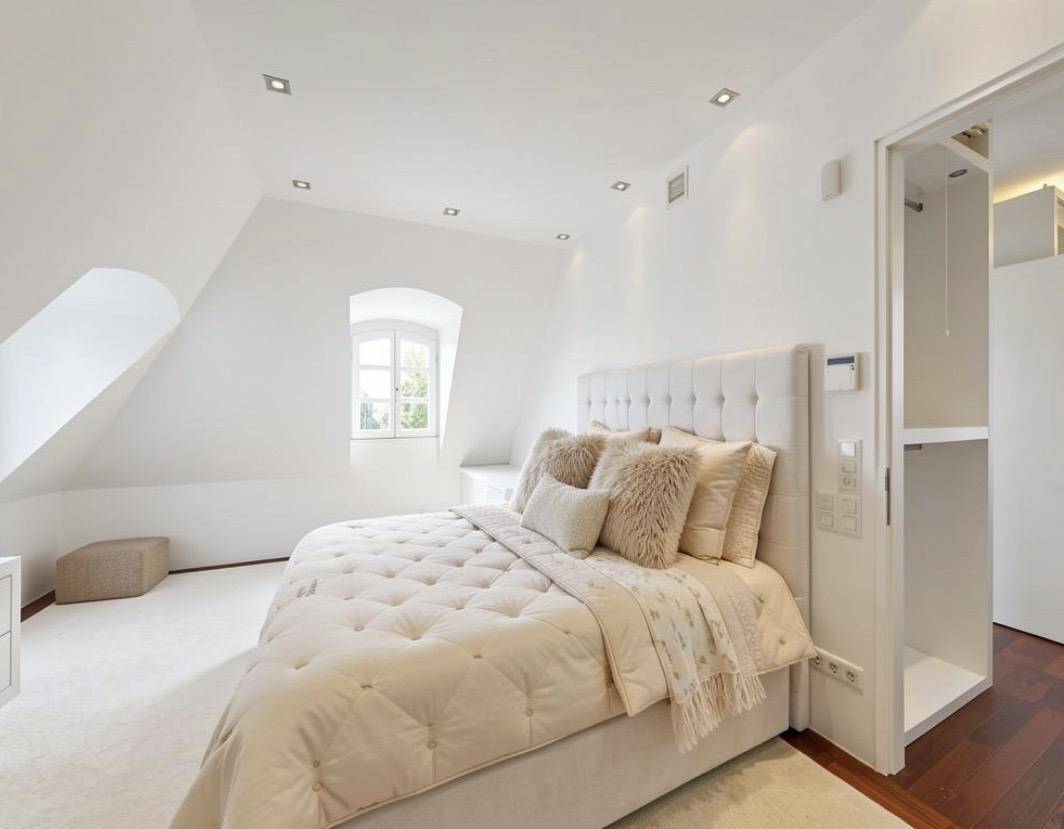 Helles Schlafzimmer im Dachgeschoss mit Dachschräge, kleinem Fenster und begehbarem Kleiderschrank.