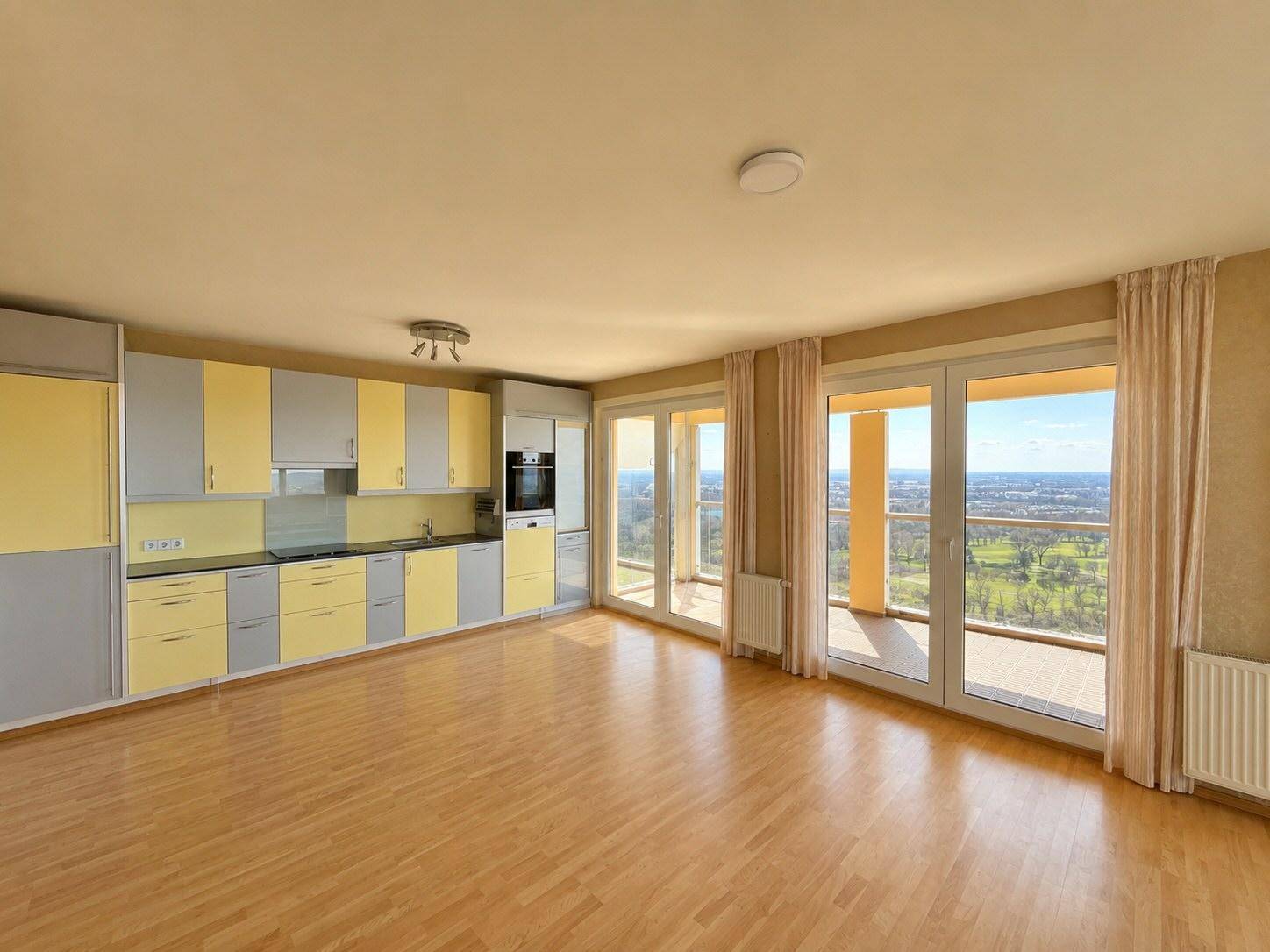 Offene Küche mit gelb-grauen Schränken, integrierten Geräten und Zugang zum Balkon mit Aussicht.