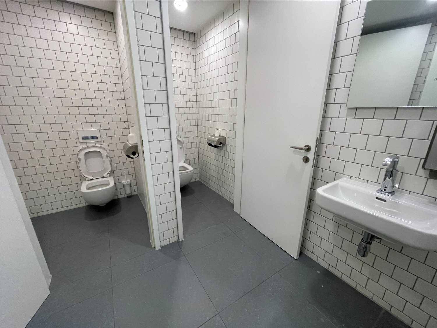 Helle Toilettenräume mit weißen U-Bahn-Fliesen, modernen Toiletten und Waschbecken.