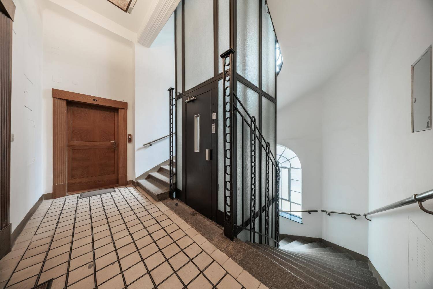 Historisches Treppenhaus mit Aufzug, Holzvertäfelung und Fliesenboden in einem Altbau.