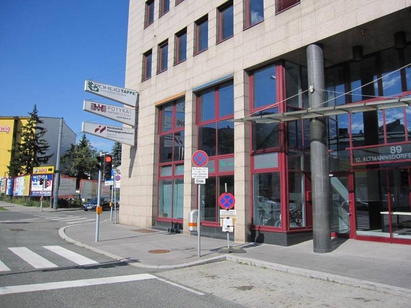 Ecke eines Geschäftsgebäudes mit großen Fenstern, Verkehrsschildern und einer Ampel an einer belebten Straßenkreuzung.