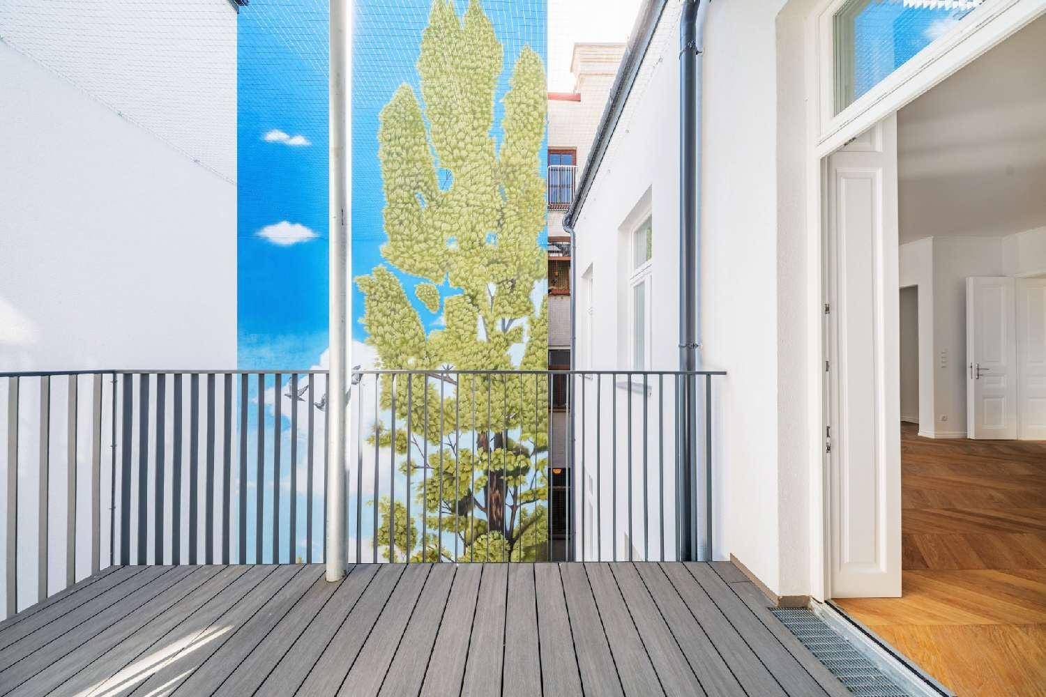 Heller Balkon mit Holzdielen und Blick auf eine künstlerisch gestaltete Fassade.